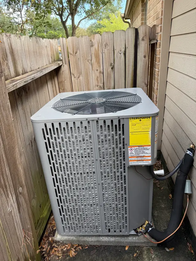 A newly installed grey condenser on its pad beside a fenced side yard in Spring