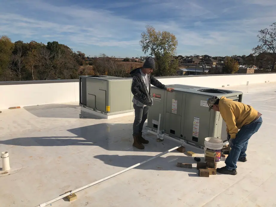 Two Douglas Mechanical crew setting Trane rooftop units on a white membrane roof under a blue sky